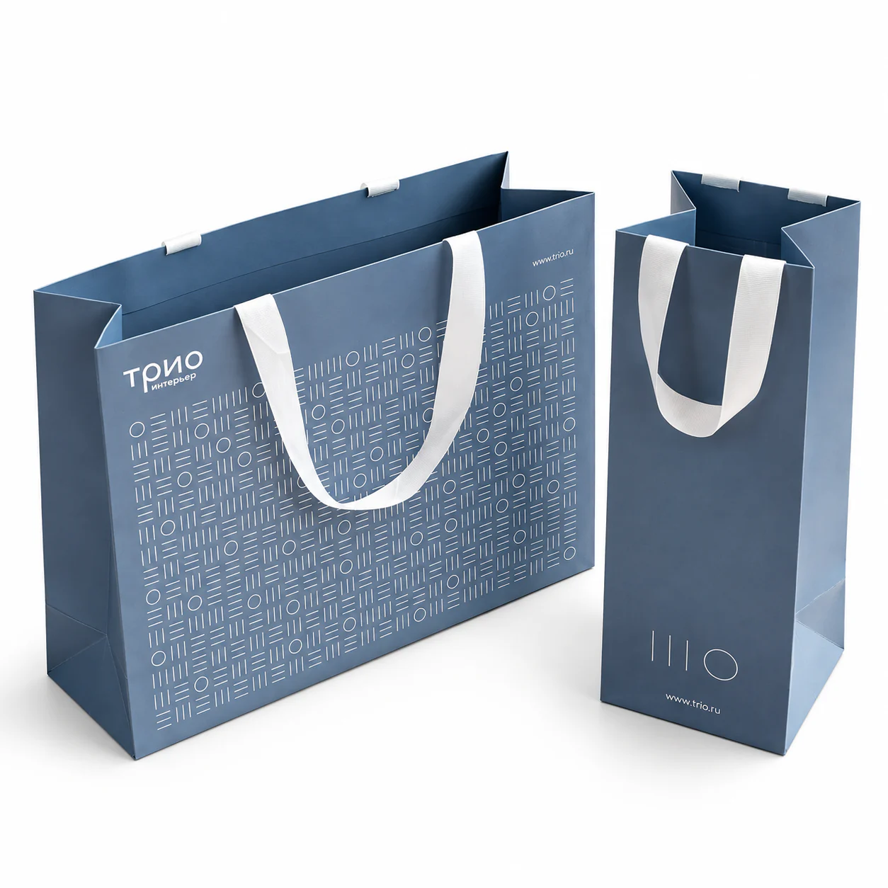 Three-quarter view of two blue paper bags in different proportions with white ribbon handles secured at the folded tops.