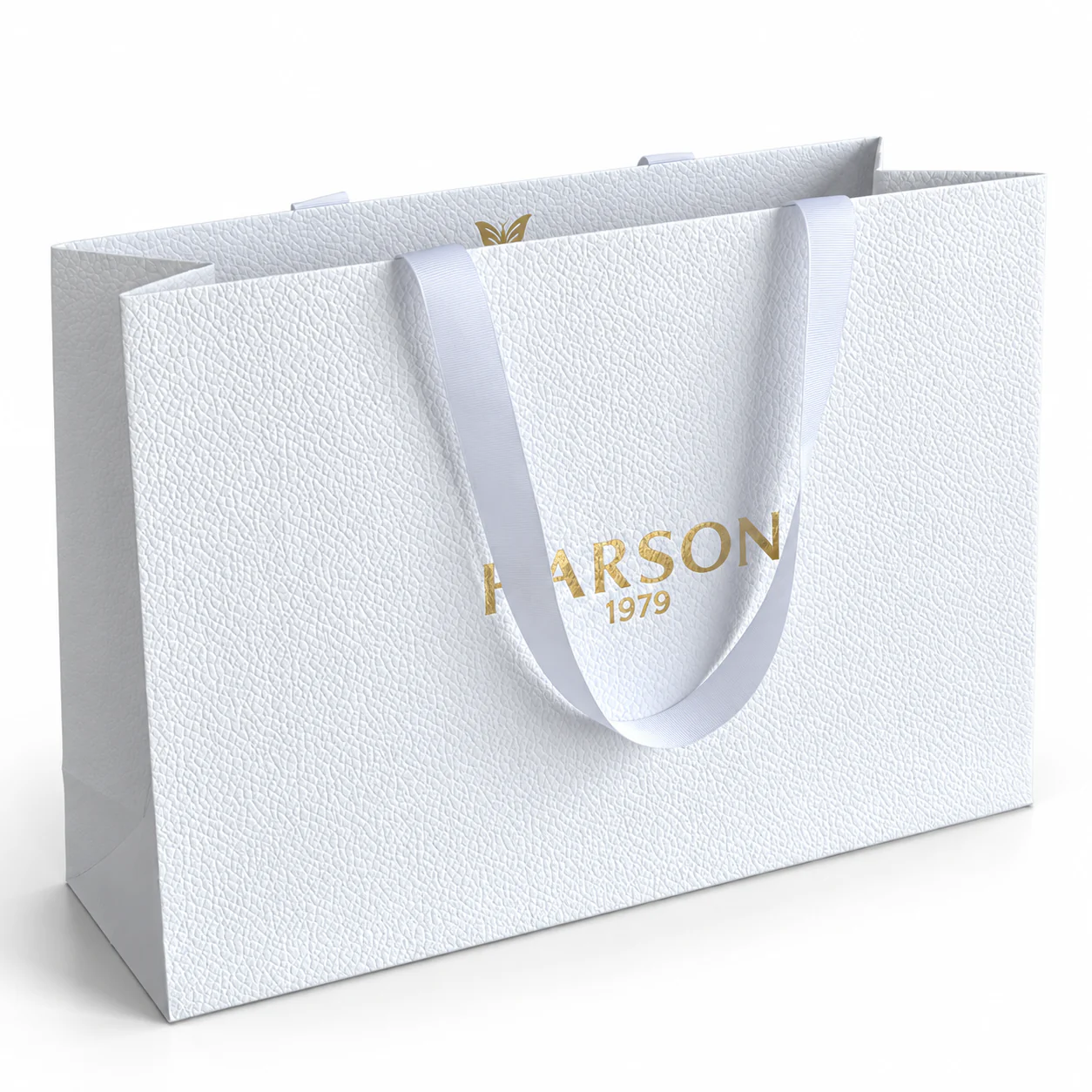 Three-quarter view of a textured white paper bag with white ribbon handles and metallic gold artwork.