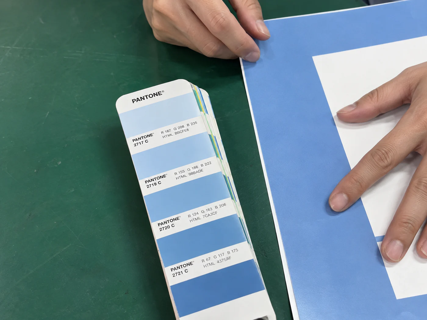 Hands holding a blue printed sheet beside a fan of colour-reference swatches.