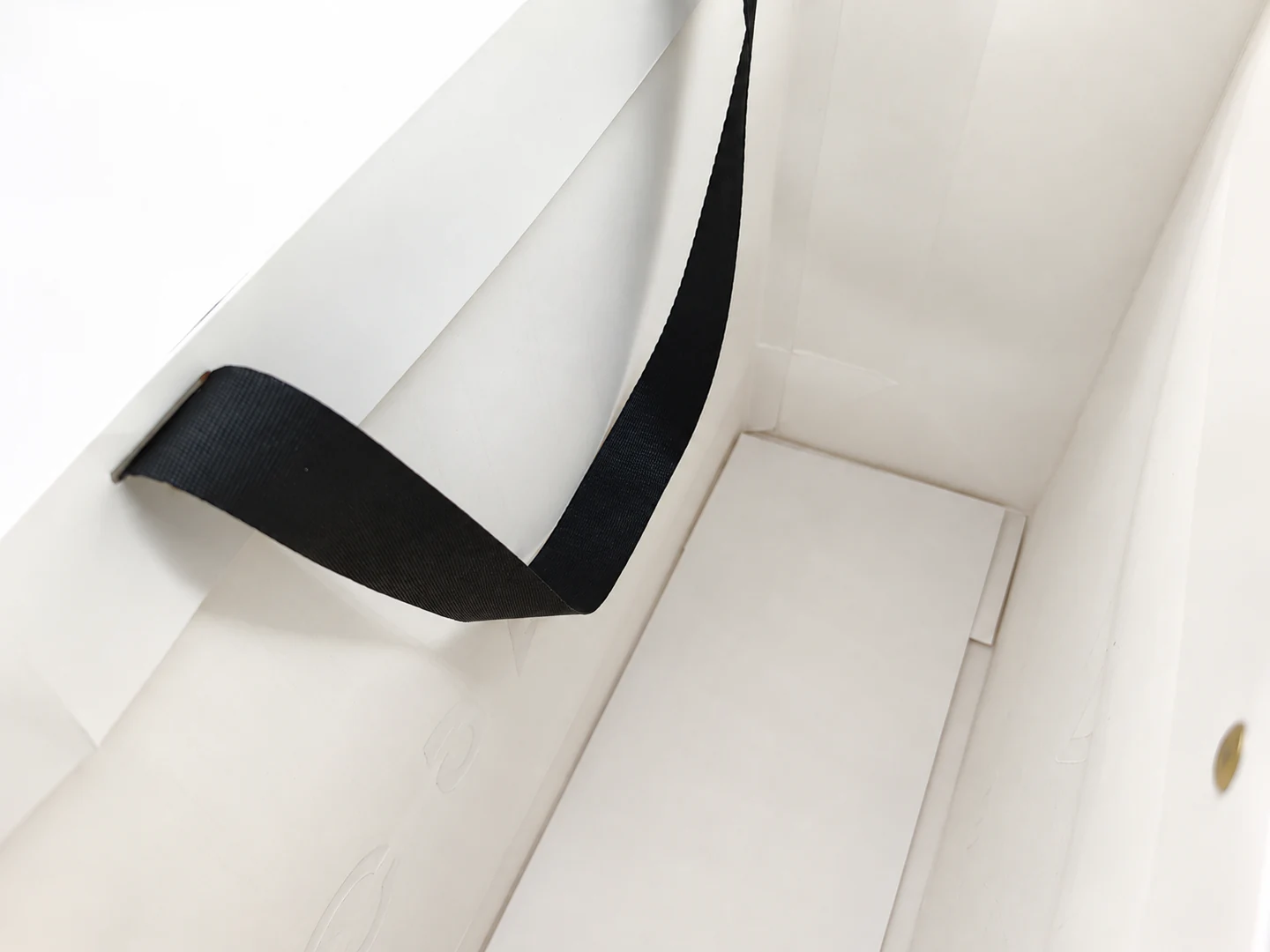 Inside a white ribbon-handle shopping paper bag, showing the separate reinforcing bottom insert.