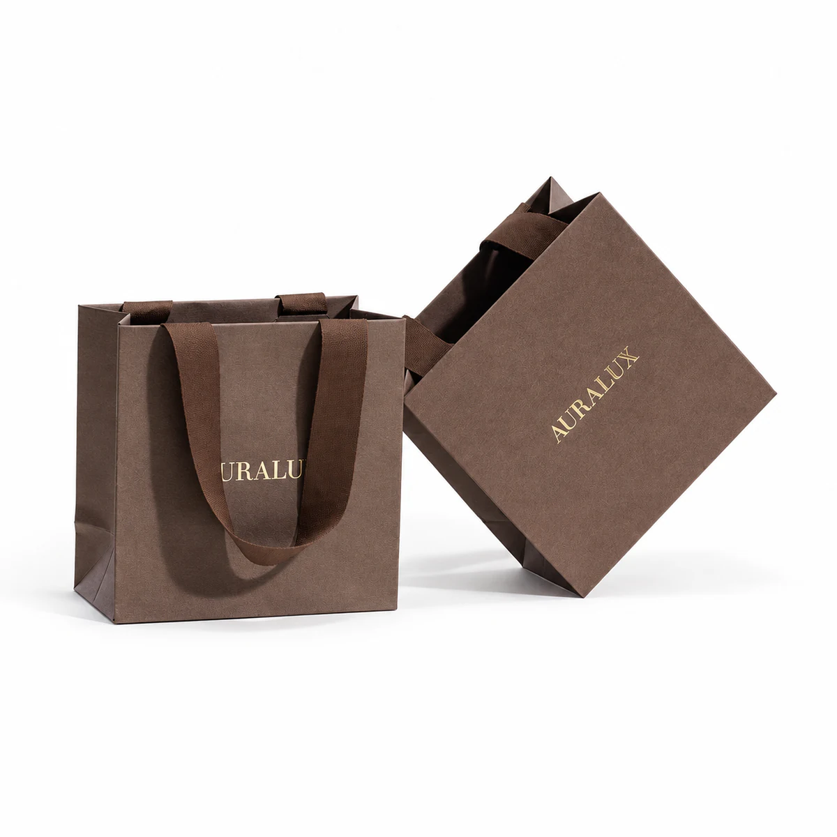 Two brown jewelry paper bags with matching wide ribbon handles and gold-coloured AURALUX lettering on a white surface with soft shadows.
