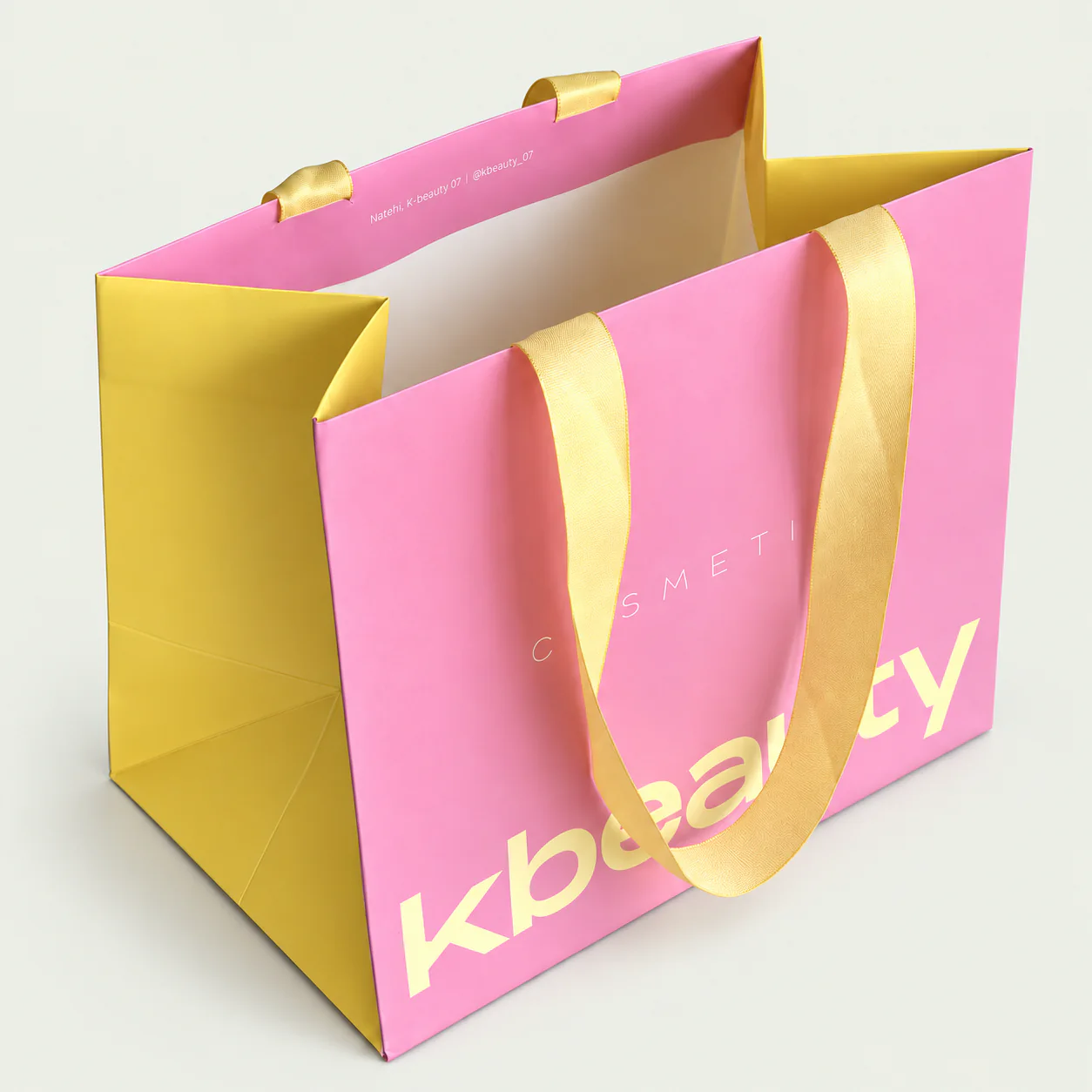 Three-quarter view of a pink paper bag with gold ribbon handles secured inside the folded top edge.