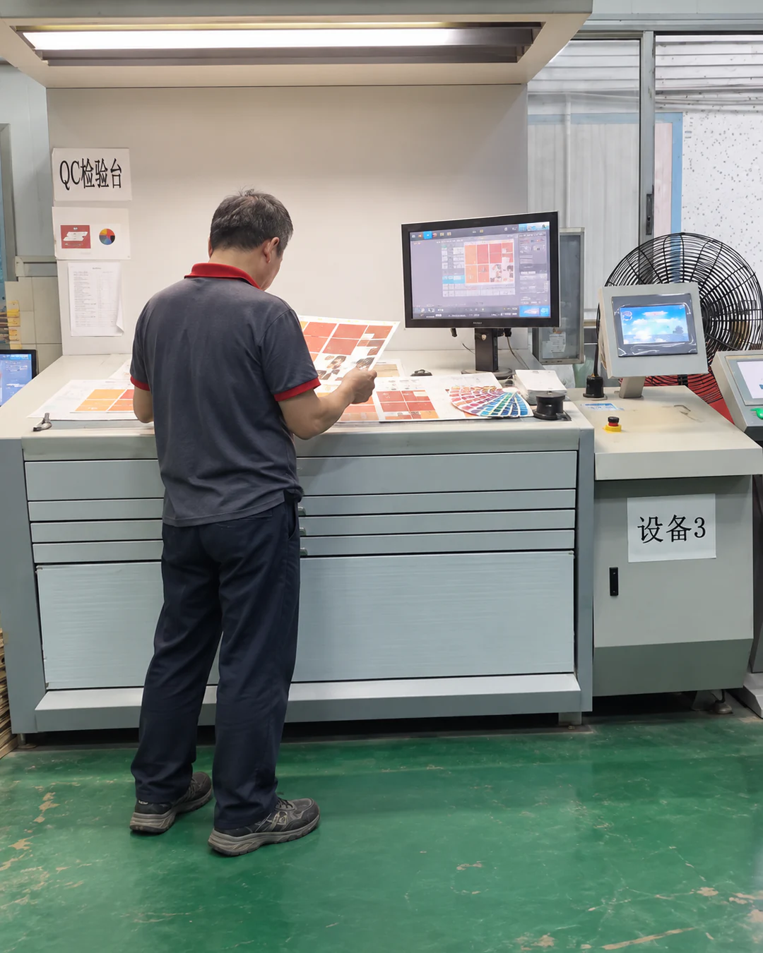 Print Batch Colour Check Worker comparing printed sheets at an illuminated print inspection desk.