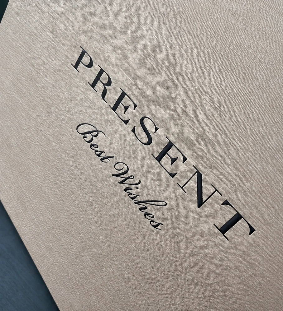 Close-up of fine linear paper texture with black PRESENT and Best Wishes lettering at an angle