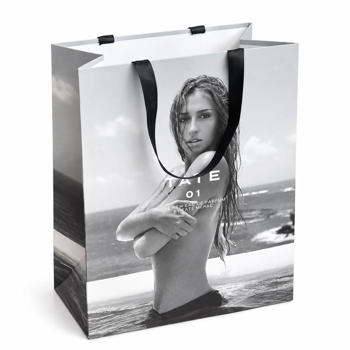 Paper shopping bag with a black-and-white portrait print and black ribbon handles.