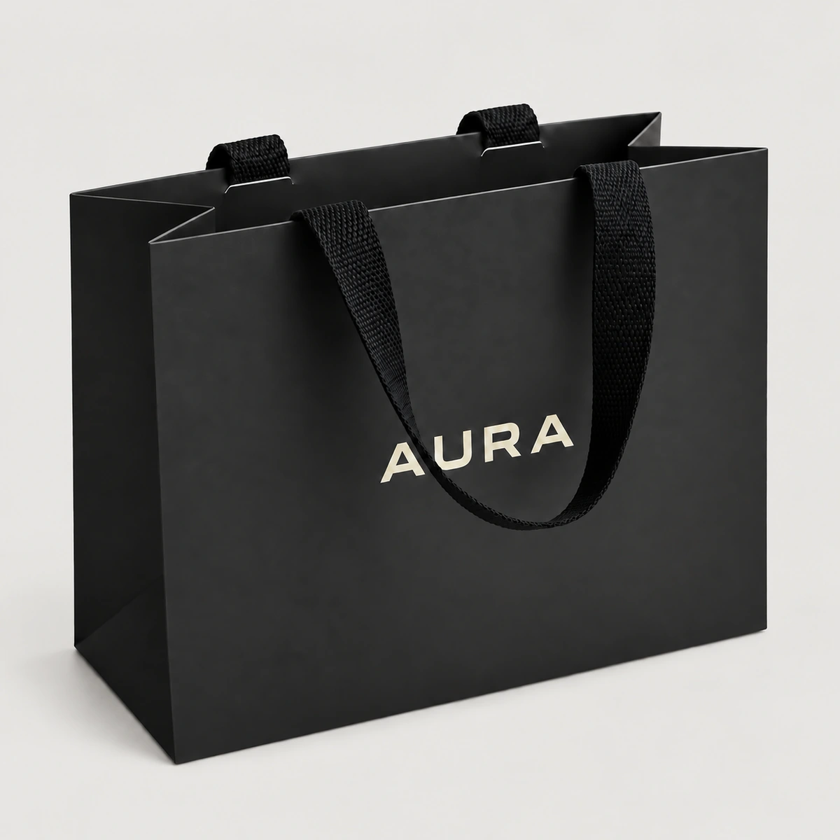 Black AURA paper bag with black woven ribbon passing over the top edge and hanging down the front