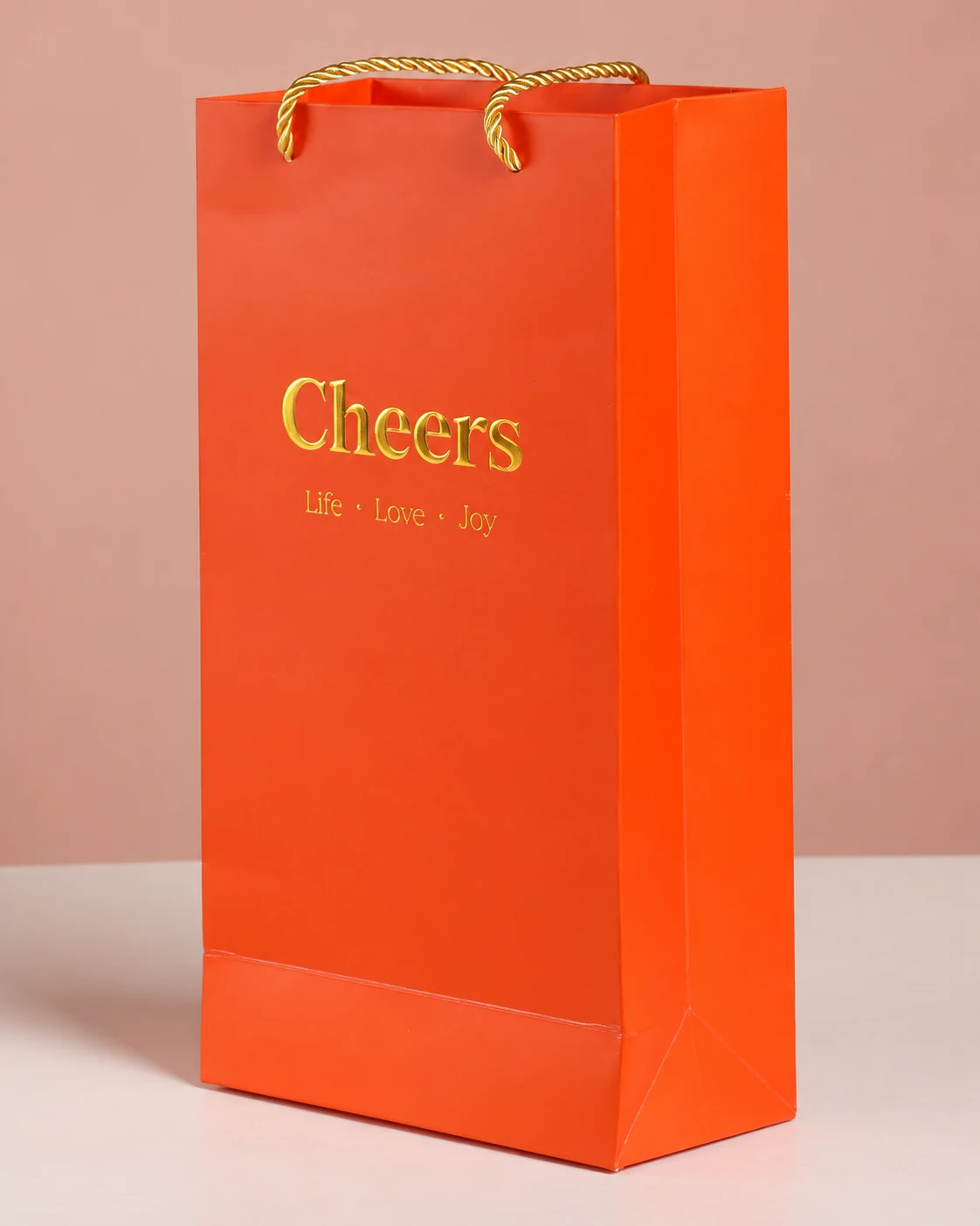 Orange wine paper bag with gold-coloured Cheers lettering, gold-coloured cord handles and a folded side gusset.