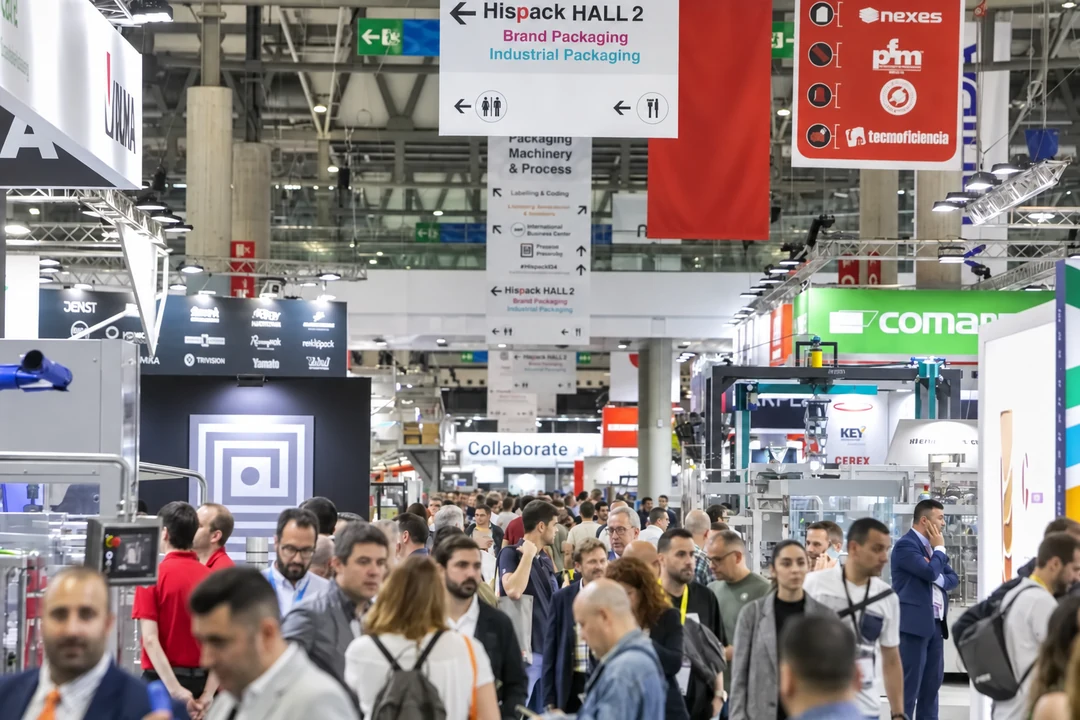 Visitors in a crowded packaging exhibition aisle beneath Hispack hall signs and hanging banners.