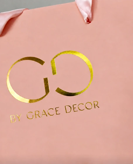 Reflective gold monogram and BY GRACE DECOR lettering on a pink paper bag