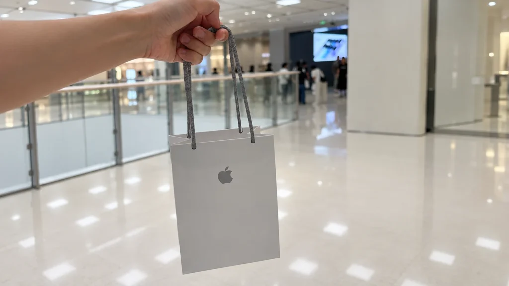 White Apple shopping bag carried by long gray knitted paper handles, with a plain front and small gray logo