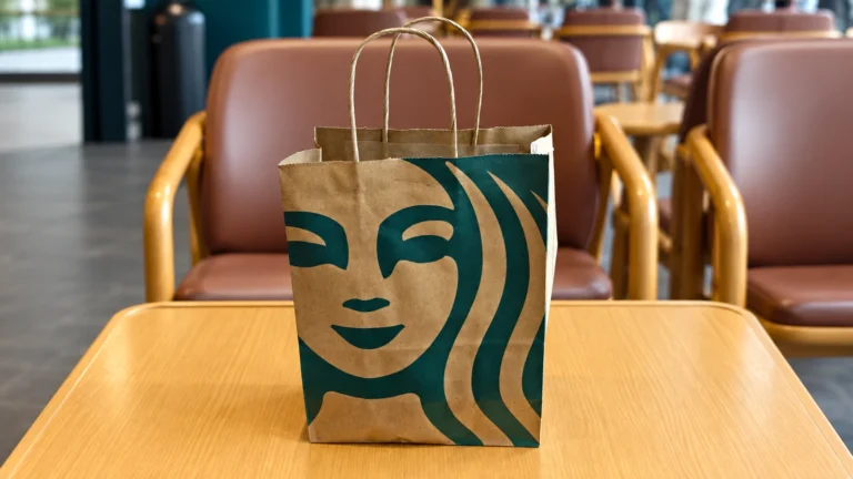 Brown Starbucks paper carrier with a large green Siren graphic and twisted handles on a café table