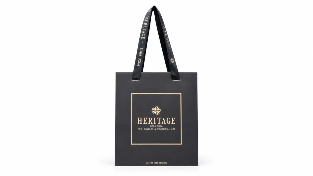 A black paper bag with gold branding and long black ribbon handles printed with matching gold lettering.