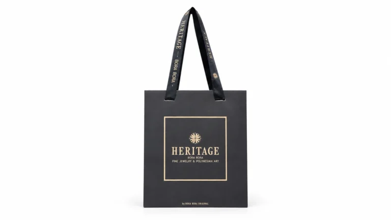 A black paper bag with gold branding and long black ribbon handles printed with matching gold lettering.