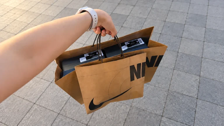 A hand carrying brown Nike kraft shopping bags with dark shoeboxes inside