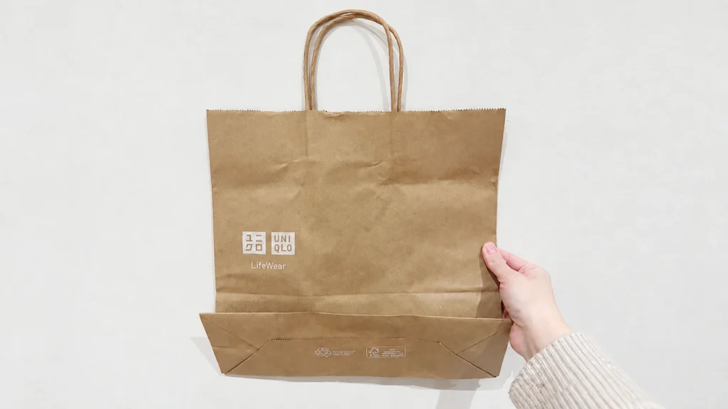 A hand holds a brown UNIQLO bag with twisted handles and the bottom panel folded upward.