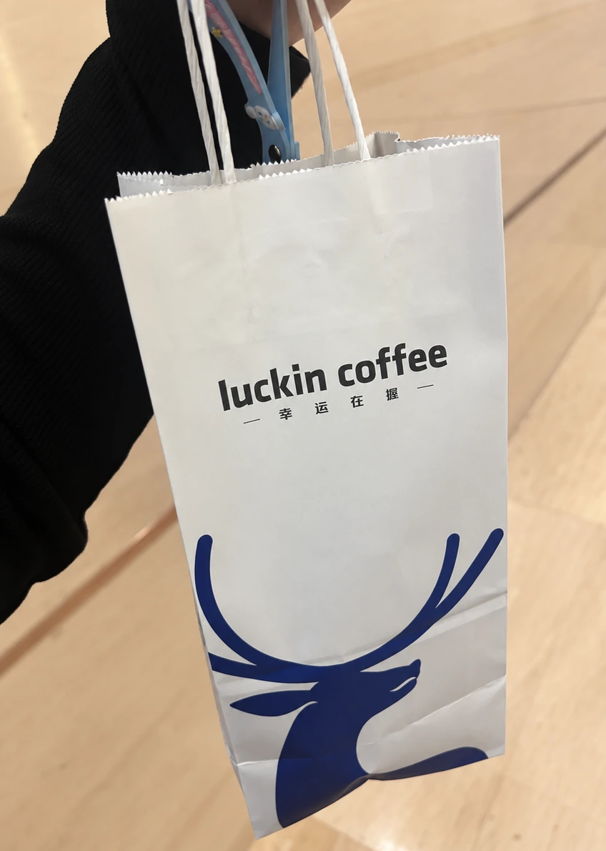 White Luckin Coffee paper bag with black lettering and a large blue deer graphic