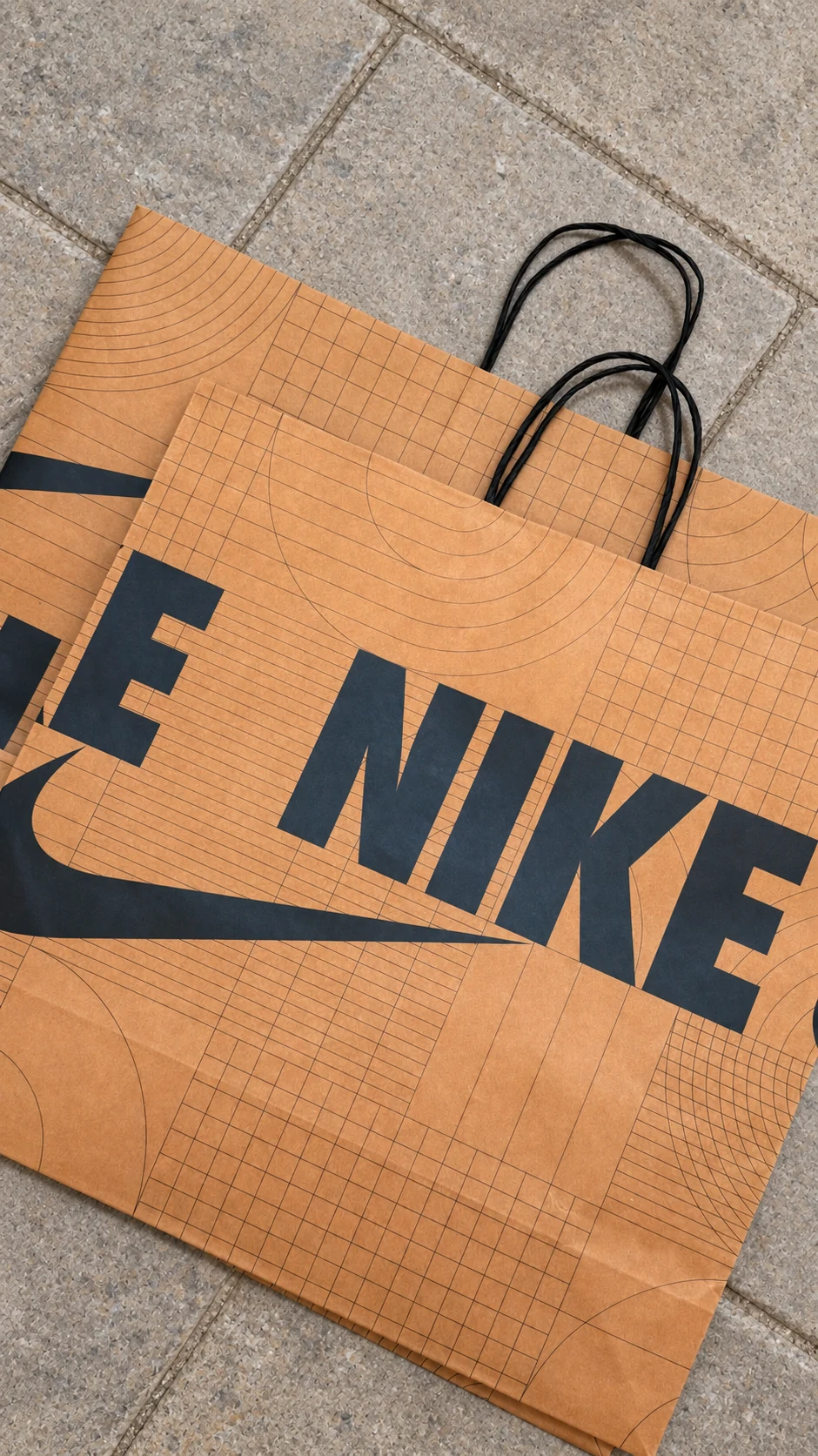 Overlapping brown Nike paper bags with bold black lettering, Swoosh graphics and fine geometric lines