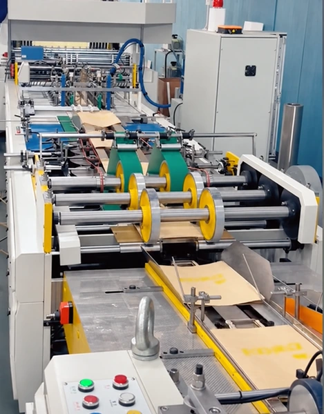 Paper bags moving through rollers and guide rails on production equipment.