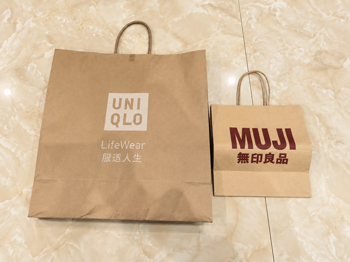 UNIQLO and MUJI brown paper shopping bags with twisted handles standing side by side