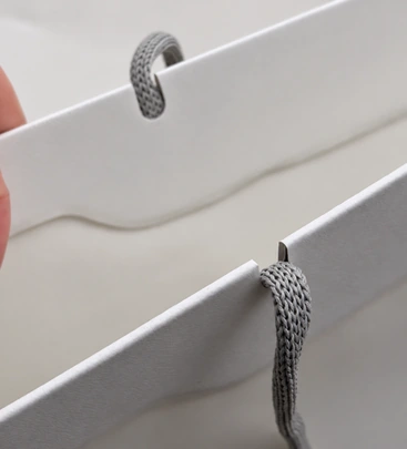 Gray paper handle meeting the folded upper edge of a white Apple shopping bag