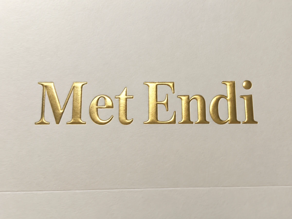Close-up of raised gold Met Endi lettering showing shaped edges on cream paper