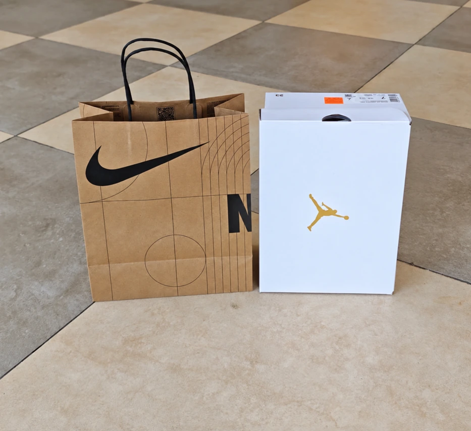 Small upright Nike kraft paper bag beside a white shoebox with a gold Jumpman logo