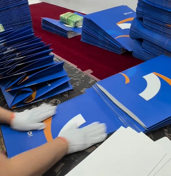 Gloved hands handling blue printed paper bags beside stacked bags on a worktable.