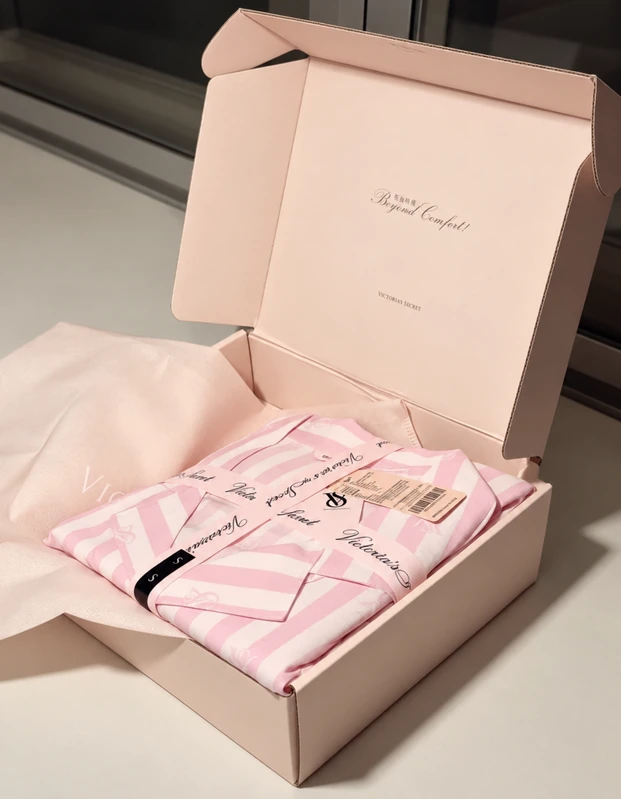 An open blush-pink Victoria's Secret box containing folded striped clothing and inner wrapping.