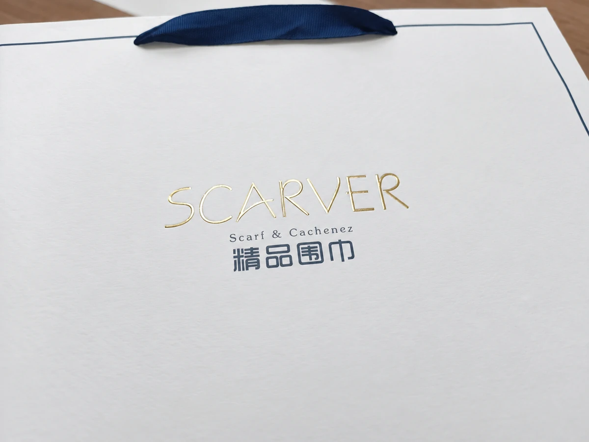 Fine gold SCARVER lettering above smaller dark printed text on a light paper bag
