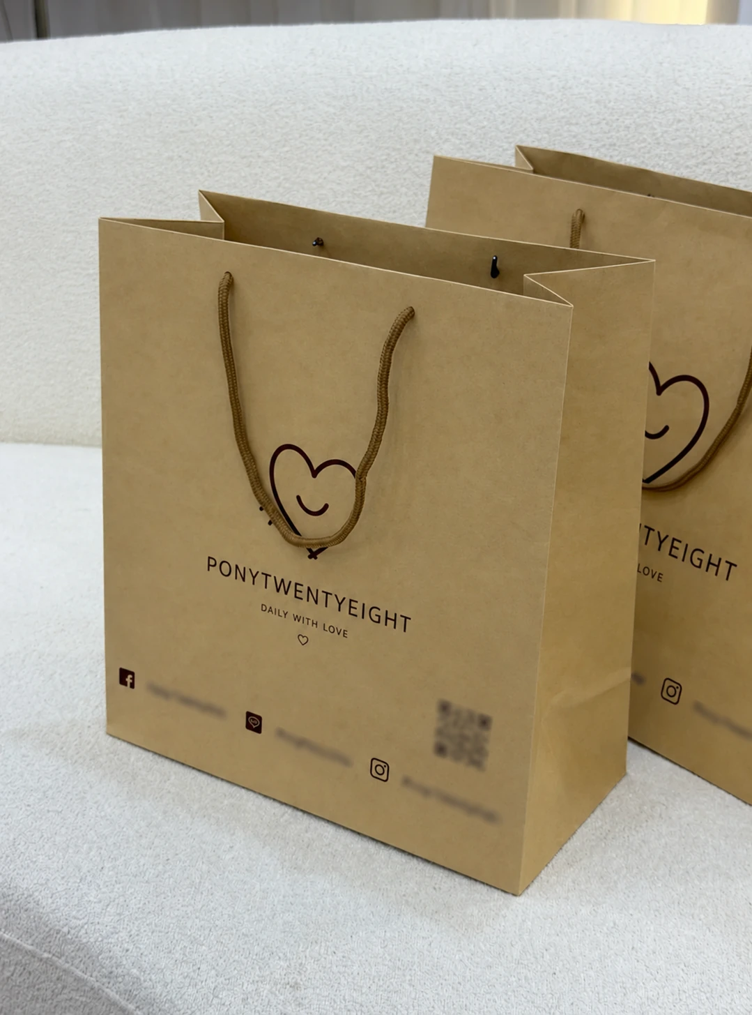 Brown PONYTWENTYEIGHT paper bags with heart logos, rope handles and blurred contact details and QR code below the main branding.
