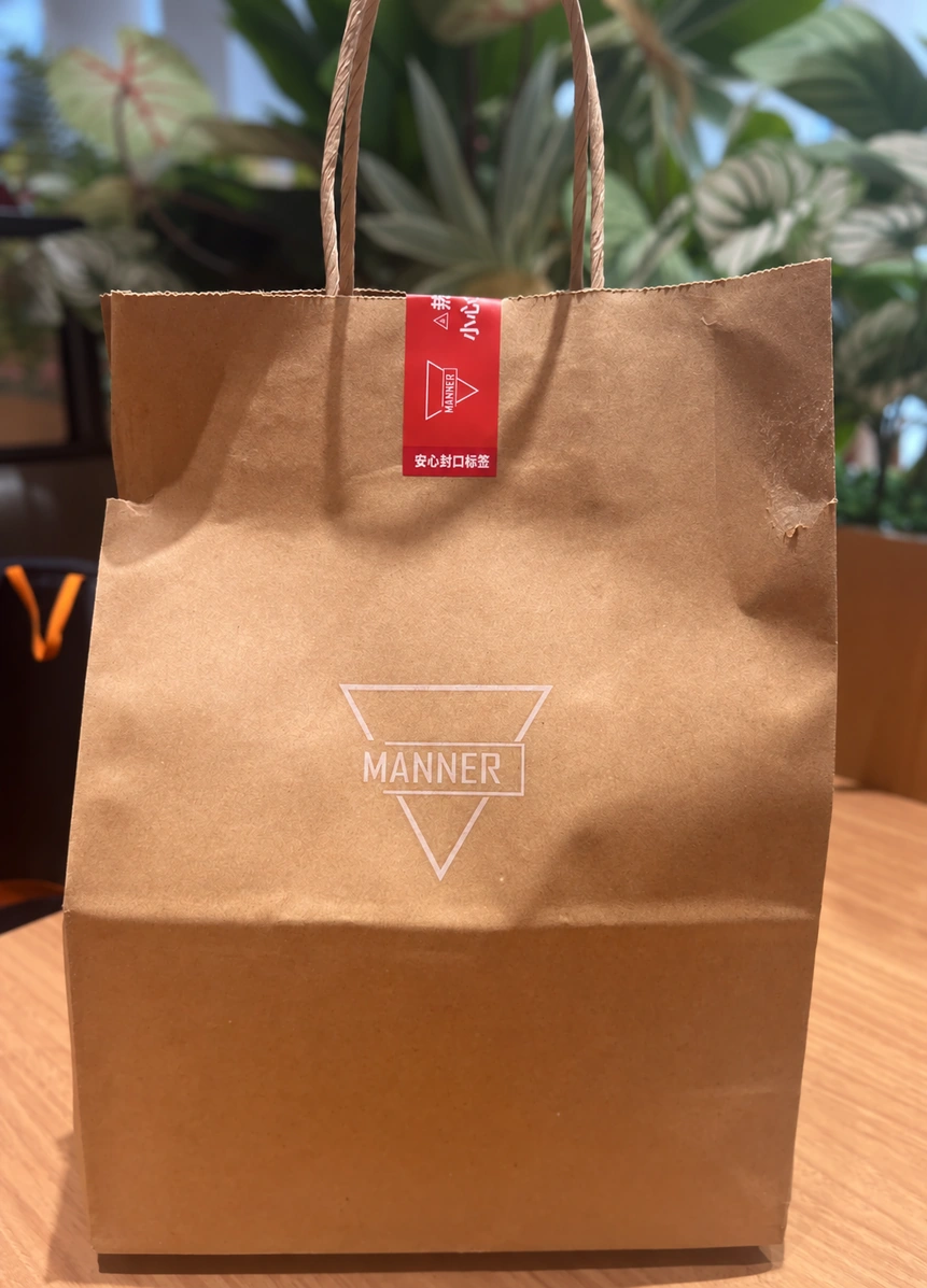 Brown MANNER paper bag with a white outlined logo and a red label across the top opening