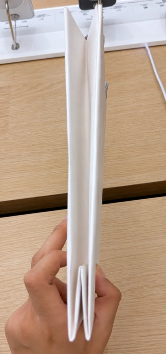 Narrow side view of a flattened Apple paper bag showing paper layers gathered at the bottom