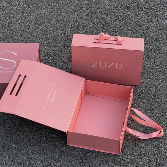 Open and closed pink handled boxes, including a ZUZU-branded box, arranged on a grey carpet.