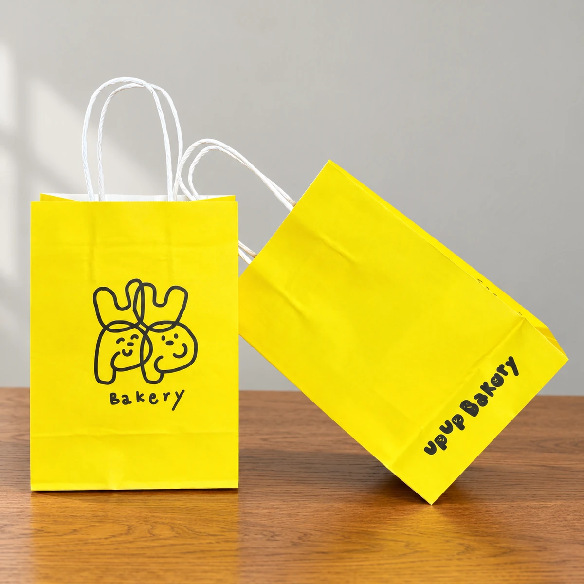 Two yellow bakery bags with white twisted handles and black printed branding