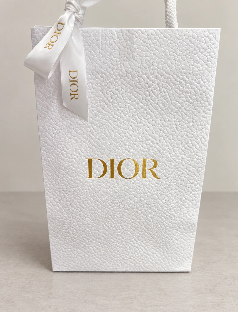 White Dior-branded reference bag with pronounced surface texture, gold-colored lettering and a tied ribbon
